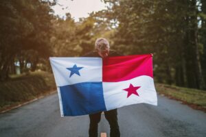 A man proudly holds the Panama flag on a quiet road surrounded by nature, symbolizing patriotism and national pride.