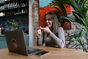 Smiling woman using sign language during a video call on a laptop in a stylish indoor setting.