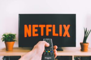 A hand holding a TV remote in front of a screen with Netflix, perfect for streaming and movie night themes.